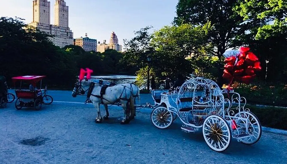 A horse-drawn carriage adorned with red bows and a floral arrangement stands in a park-like setting with a backdrop of tall buildings suggesting an urban environment