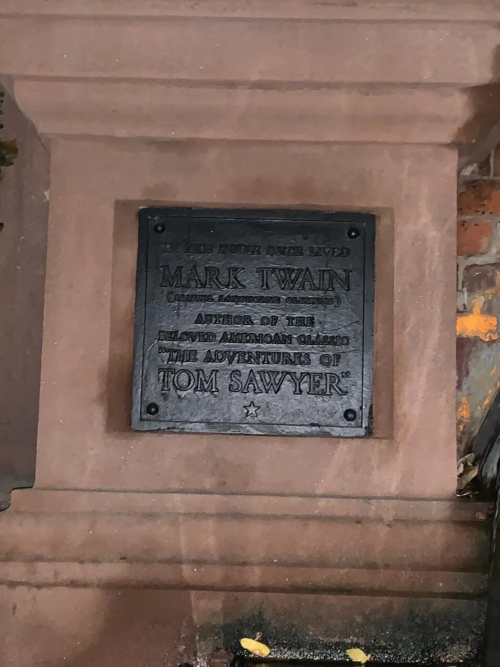 The image shows a commemorative plaque honoring Mark Twain the author of the beloved American classics The Adventures of Tom Sawyer and others affixed to a stone wall or structure