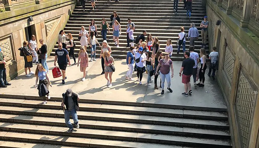 A group of people is seen ascending and descending a wide outdoor staircase on a sunny day