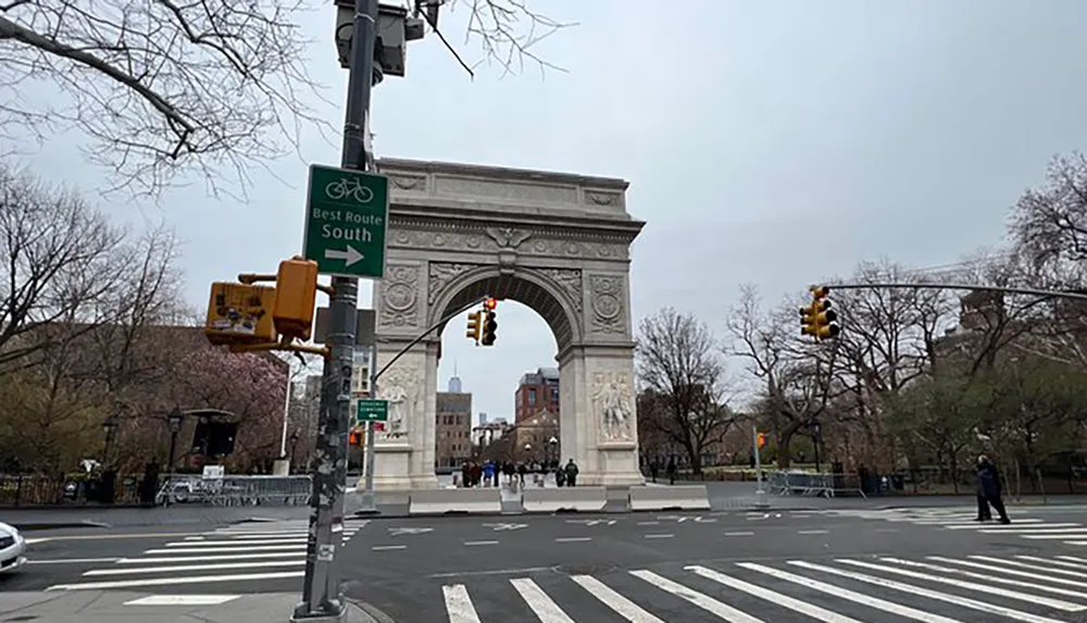 The image shows the Washington Square Arch located at the northern entrance of Washington Square Park in Manhattan with a bicycle route sign in the foreground and a skyscraper faintly visible in the distance