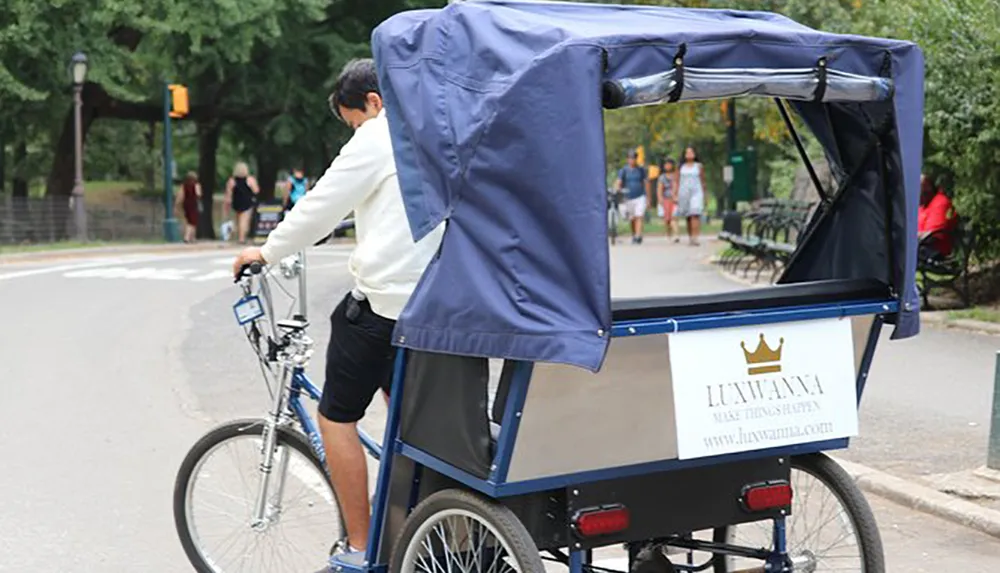 A pedicab driver stands by his vehicle waiting for passengers in a park with pedestrians in the background