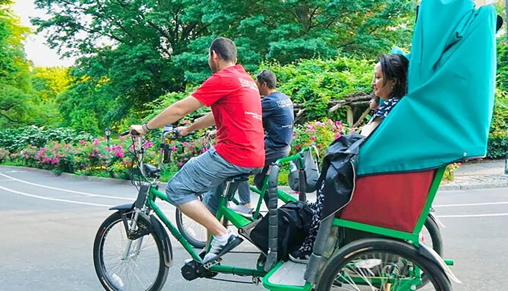 A man pedals a rickshaw with a passenger onboard through a lush park setting