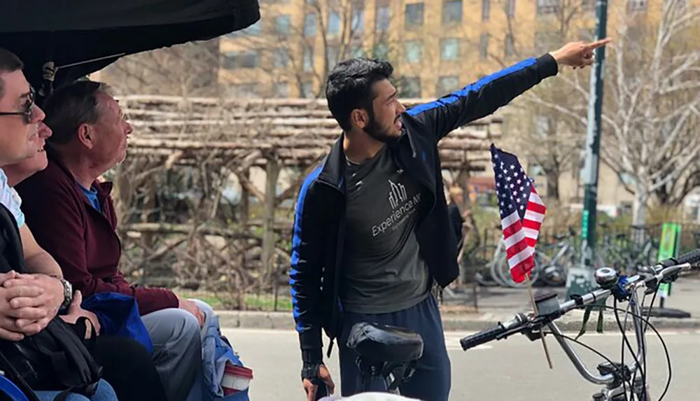 A tour guide is pointing out a site of interest to two passengers in a pedicab adorned with an American flag