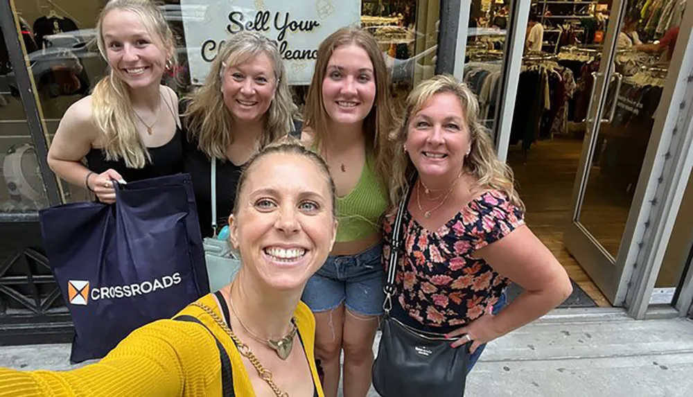 A group of five smiling women takes a selfie in front of a clothing store