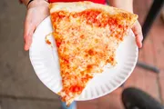 A person is holding a plate with a large slice of cheese pizza.