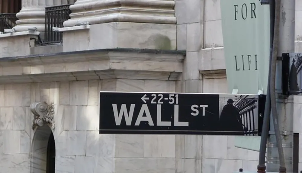 The image shows a directional sign for Wall Street with building numbers 22-51 against a background of a stone building with part of a banner reading FOR LI FI