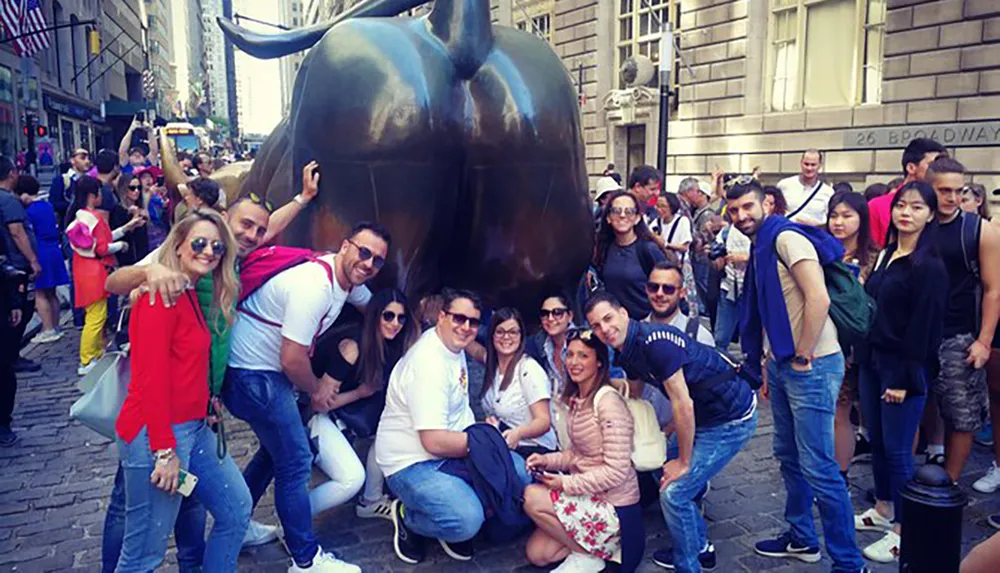 A group of cheerful people are posing for a photo with the Charging Bull sculpture in New York Citys financial district