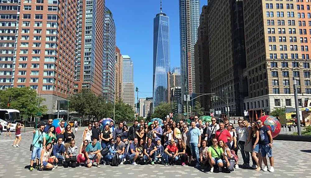 A large group of people are posing for a photo on a sunny day with skyscrapers in the background including the World Trade Center in New York City