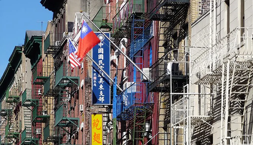 The image shows a bustling city street lined with buildings featuring external fire escapes and several flags including the American and Taiwanese flags indicative of a diverse urban neighborhood