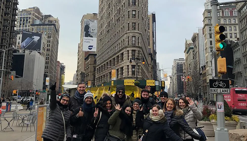 A group of people is posing and smiling at the camera in front of the Flatiron Building in New York City