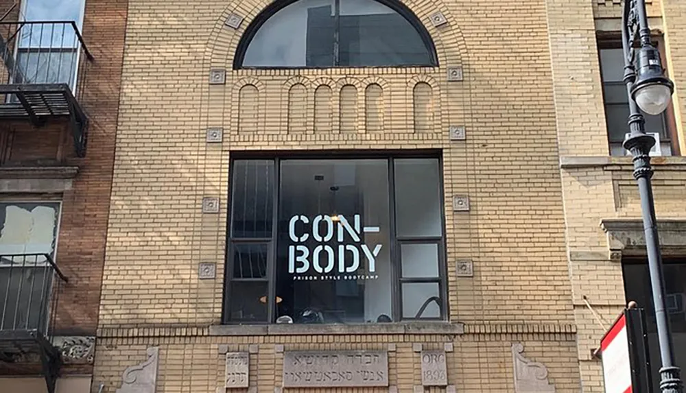 The image shows the facade of a building with a large window featuring the words CONBODY PRISON STYLE BOOTCAMP suggesting a workout facility offering a fitness program inspired by prison routines