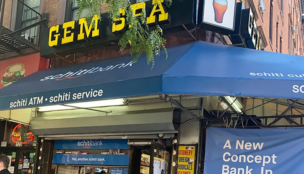 The image shows the exterior of a business with humorous alterations to its sign that make it appear to say schiti ATM schiti service and schitibank which are playful modifications of a real banks branding