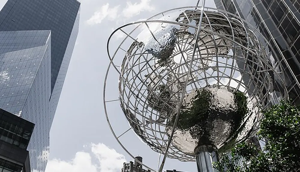 The image shows a large metallic globe sculpture in front of modern skyscrapers set against a partly cloudy sky