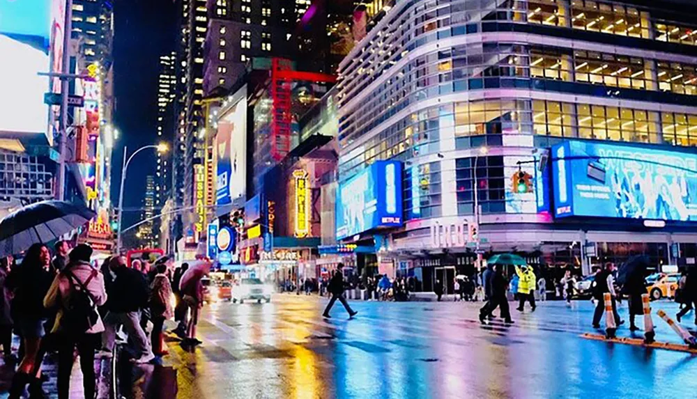 A vibrant night scene of a busy urban street with bright billboards and pedestrians some holding umbrellas indicative of a bustling city life possibly Times Square in New York