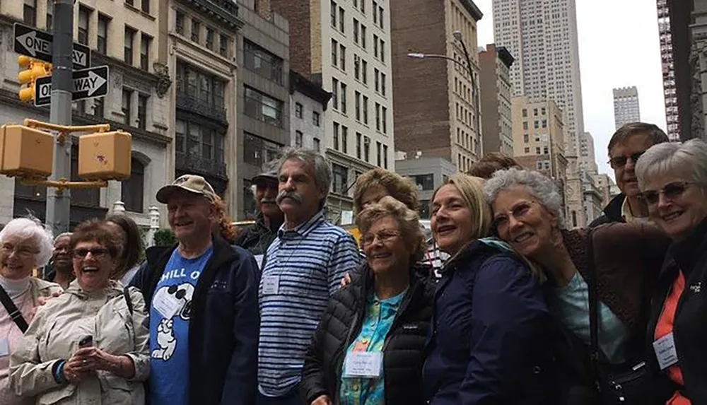 A group of smiling people possibly tourists gather closely together on a city street with tall buildings in the background and a street sign overhead