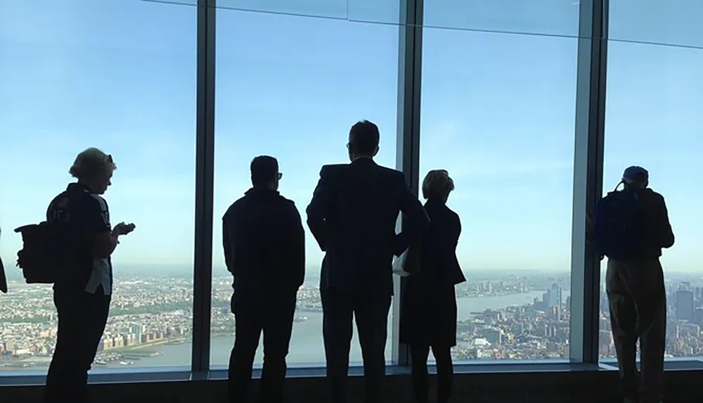 Five silhouetted figures stand before a large window overlooking a cityscape with the bright daylight casting them in shadow