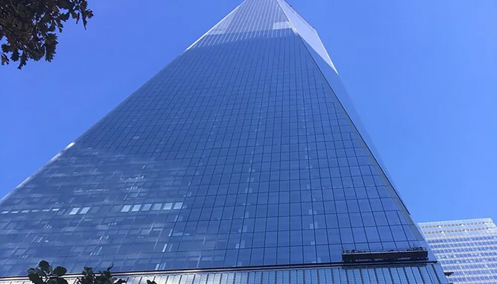The image shows a towering skyscraper with a distinctive angular structure and reflective glass facade set against a clear blue sky
