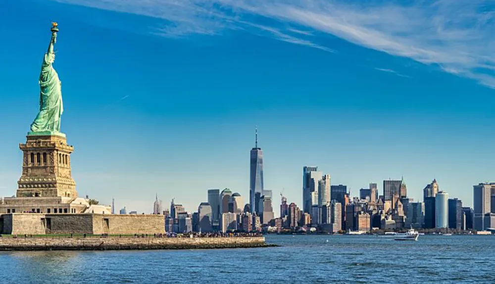 The image features the Statue of Liberty in the foreground with the skyline of Lower Manhattan including the One World Trade Center in the background under a clear blue sky