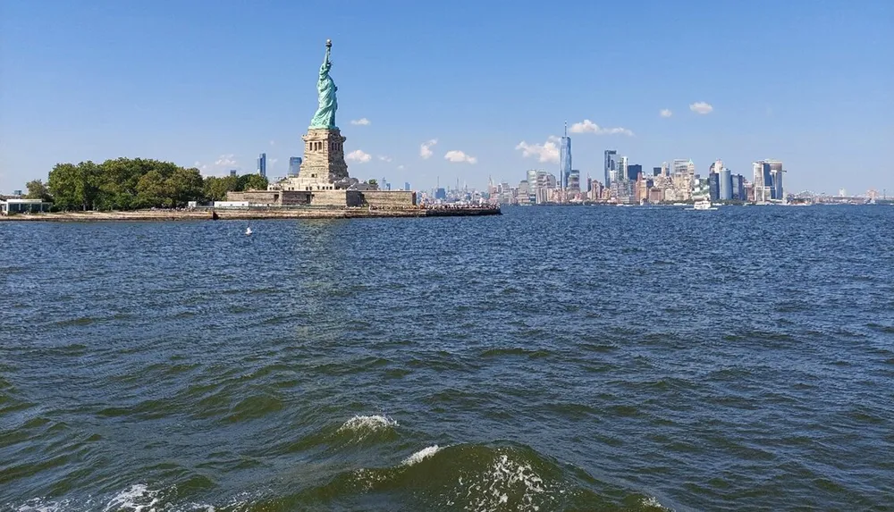 The image shows the Statue of Liberty with the New York City skyline in the background viewed from the water