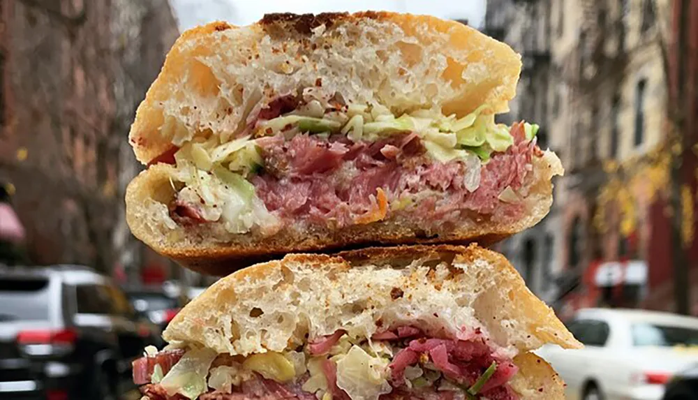 A split corned beef sandwich with coleslaw on a crusty bread held with a backdrop of an urban street scene