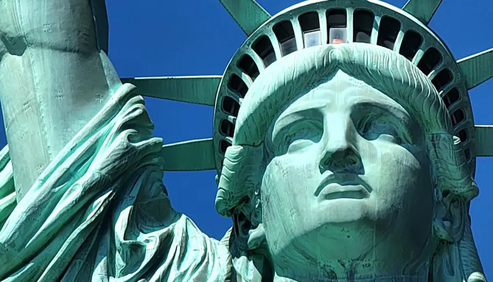 The image shows a close-up view of the Statue of Liberty against a clear blue sky
