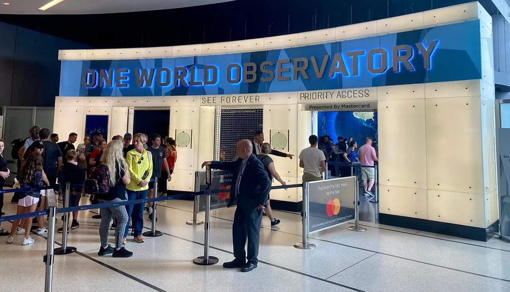 Visitors line up at the entrance of One World Observatory with a sign indicating Priority Access Presented by Mastercard